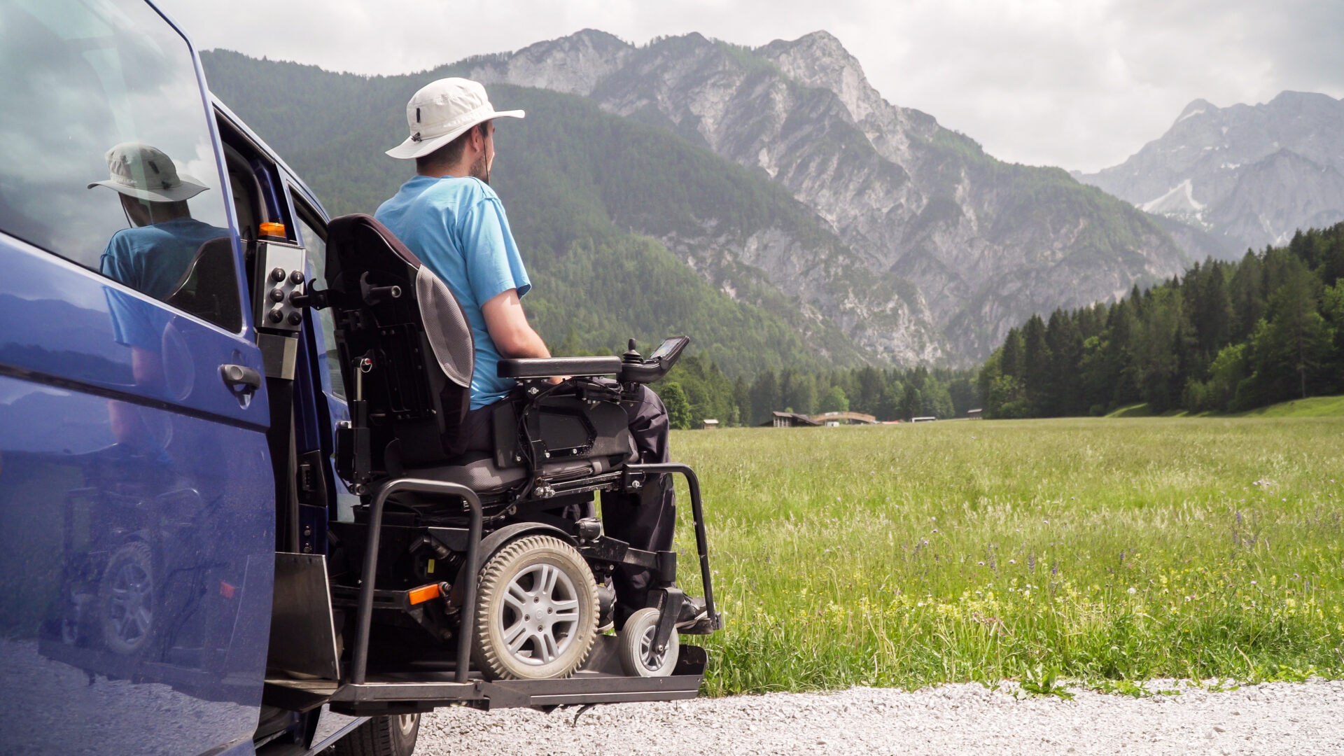 Homme en fauteuil roulant électrique sortant d'un véhicule adapté via une plateforme élévatrice.